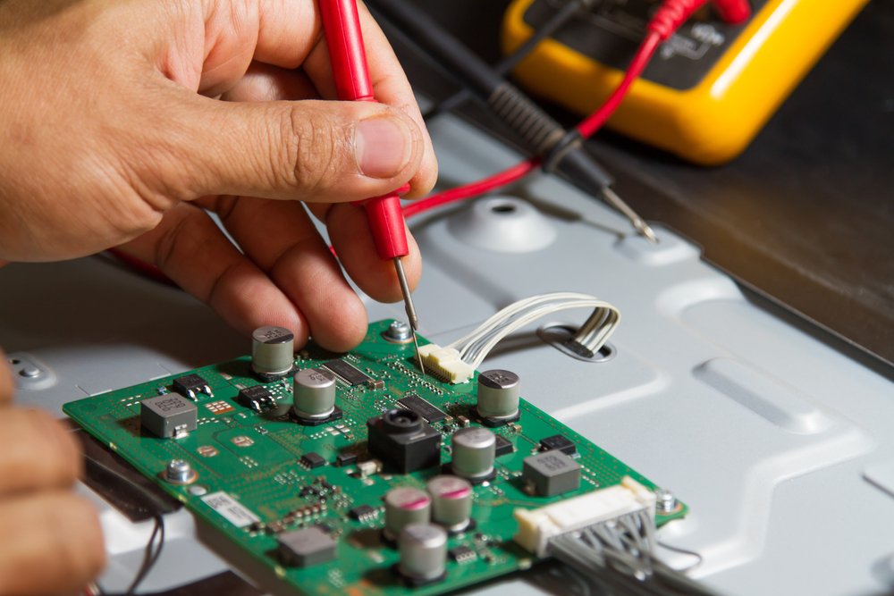 A person uses a multimeter to test a green circuit board.
